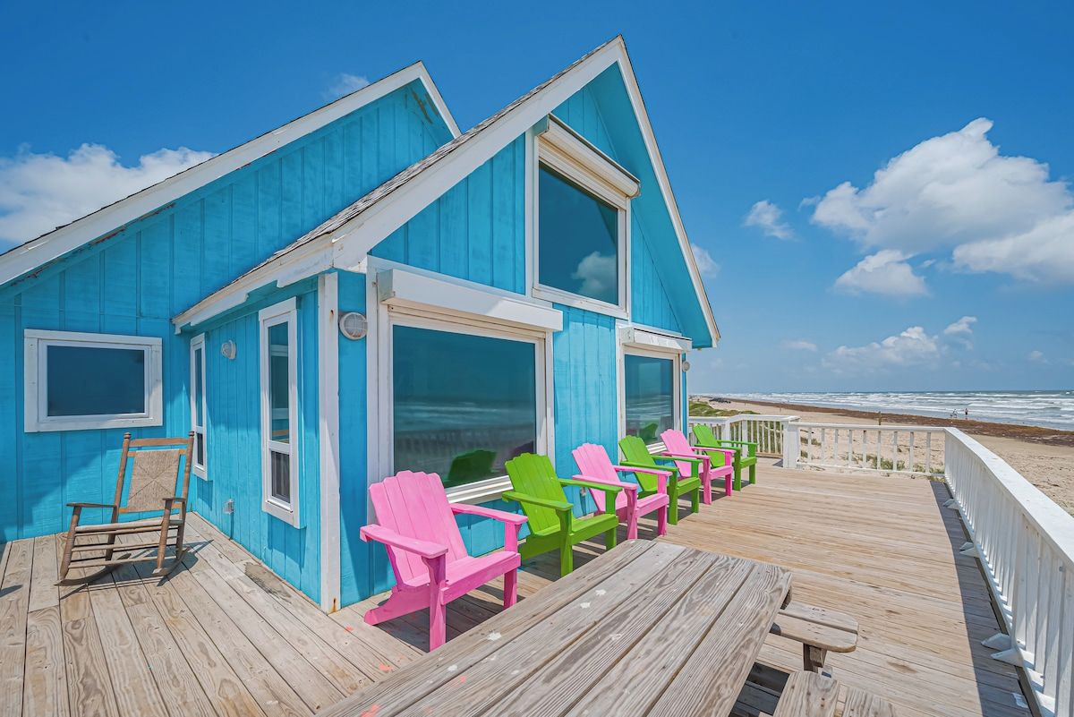 Un bâtiment bleu doté d’une terrasse et de chaises Adirondack aux couleurs vives.