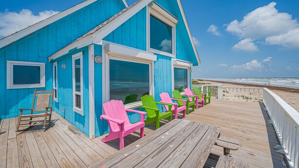 Un edificio azul con una terraza de madera y sillas Adirondack de colores.