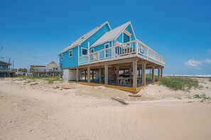 A beachfront house with a balcony, a covered porch, and a sandy beach in the background.