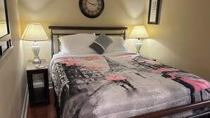 Un lit bien fait, recouvert d’une couvre-lit à motifs, deux lampes de chevet, une horloge murale et un certificat encadré accroché au mur.