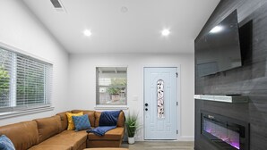 Un salon moderne avec un canapé en cuir marron, une petite table, un téléviseur à écran plat fixé au mur et une cheminée avec une façade en verre.