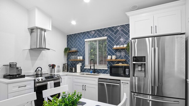 Une cuisine moderne avec des meubles blancs, des appareils en acier inoxydable et un pare-feu bleu à motifs.