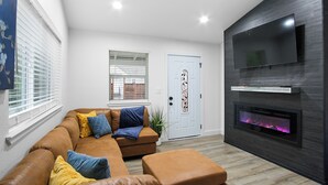 Un salon moderne avec un canapé d’angle, un téléviseur à écran plat fixé à un mur foncé et une cheminée.