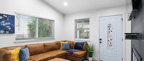 A modern living room with a brown sectional sofa, a door with decorative glass, and a potted plant.