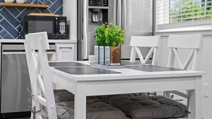 Une cuisine moderne avec des meubles blancs, un réfrigérateur en acier inoxydable, un four à micro-ondes et un distributeur d’eau. On y trouve une table à manger avec une chaise blanche et un banc rembourré.