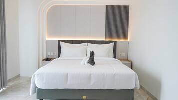 Una habitación de hotel moderna con una cama bien hecha, una mesita de noche con lámpara y un panel en la pared sobre la cama.