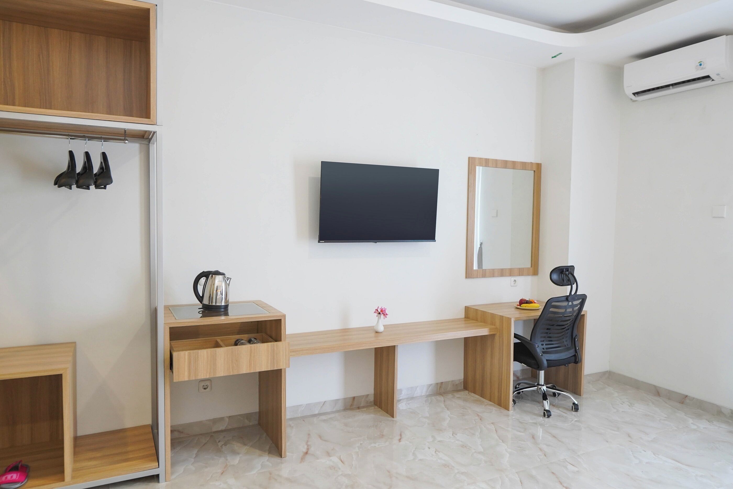Ein modernes Zimmer mit Schreibtisch aus Holz, Fernseher, Spiegel und Kleiderschrank mit Schuhen.