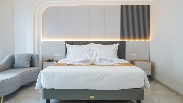Una habitación de hotel moderna con una cama grande, un sofá gris y una mesita de noche con una lámpara.