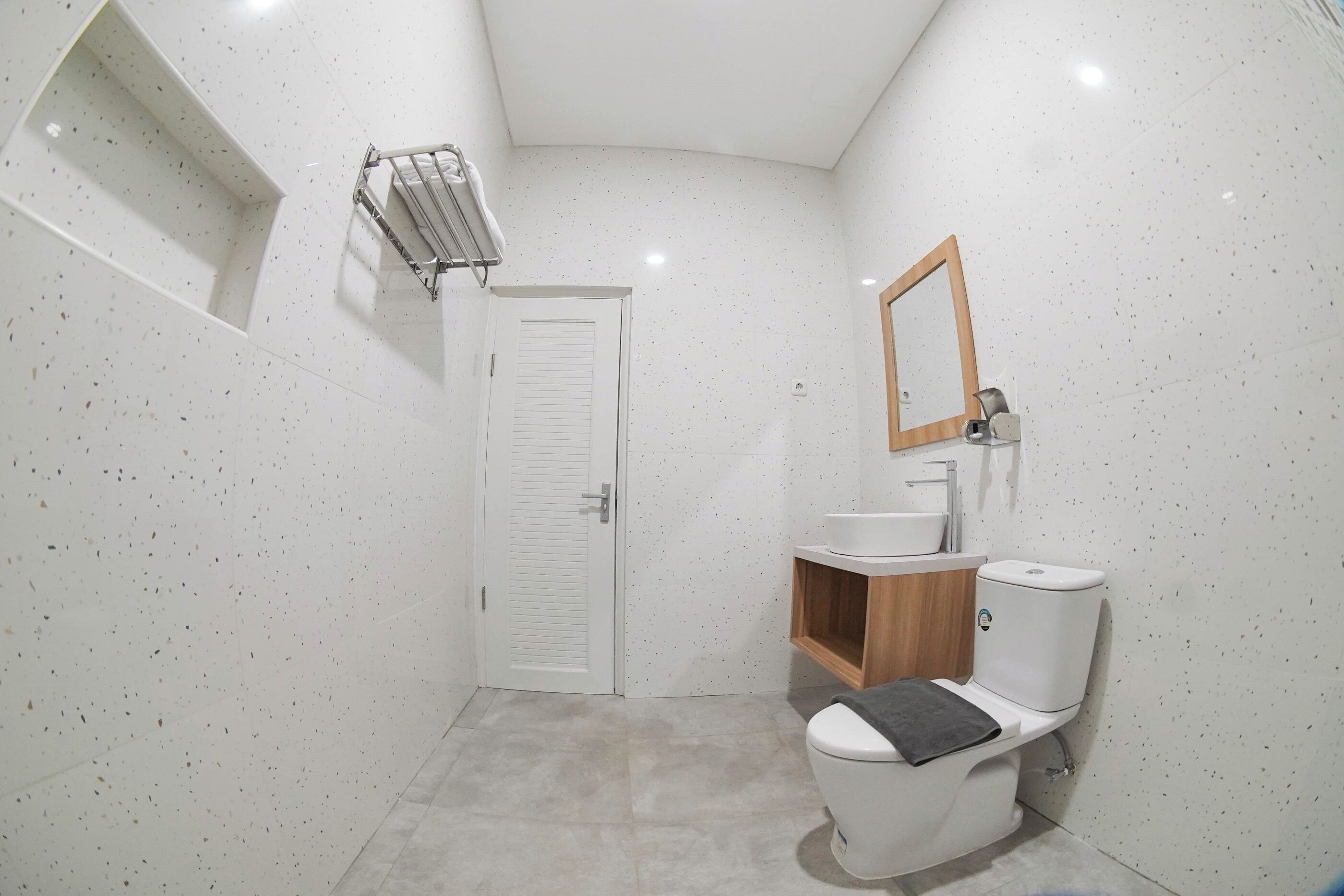A compact bathroom with a white toilet, a wooden vanity, a mirror, and a towel rack.