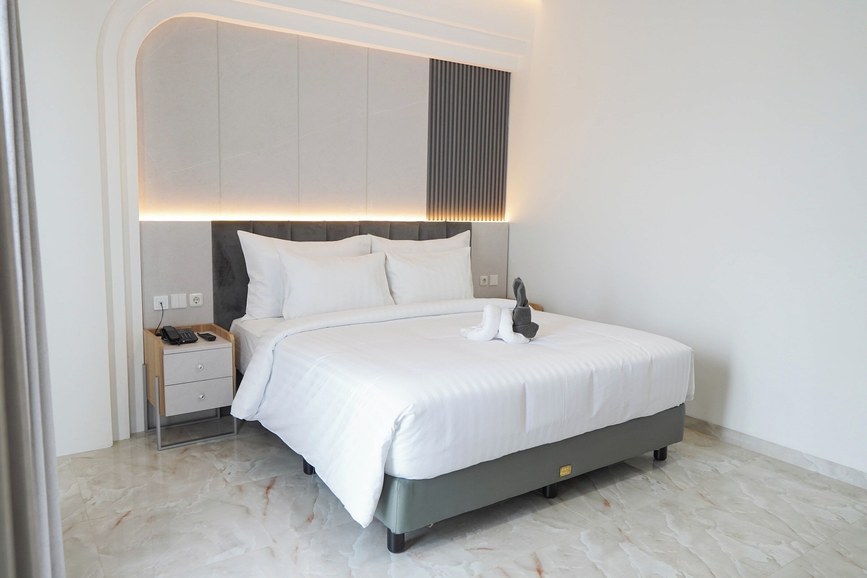 A modern bedroom with a bed, bedside table, and a wall-mounted light fixture.