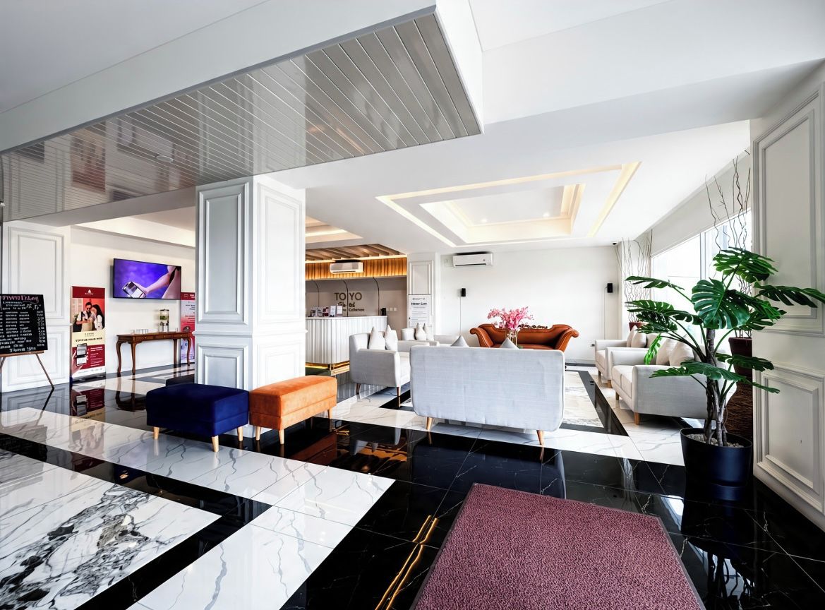 Un hall d’hôtel moderne avec un sol en marbre, des coins salon, un téléviseur et une grande plante en pot.