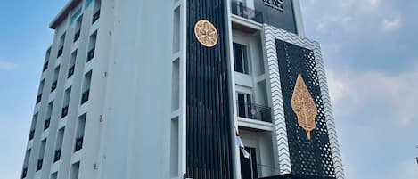 A multi-story hotel with a modern design, featuring a prominent logo on the facade and a balcony on the upper floors.