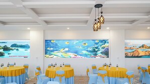 Un salón de conferencias con mesas redondas, sillas azules y amarillas, y amplios murales en la pared que representan escenas submarinas.