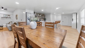 Une cuisine moderne avec des meubles blancs, une table à manger en bois et un grand vase.