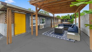 Un patio abrité avec une pergola en bois, une porte jaune et des sièges d’extérieur.