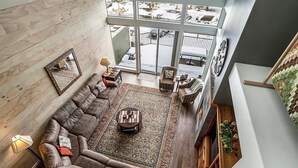 A spacious living room with a large sectional sofa, a coffee table, and a view of the outdoors through large windows. - Charming 3-bedroom townhome with WiFi, fitness room in peaceful Redmond (Redmond)