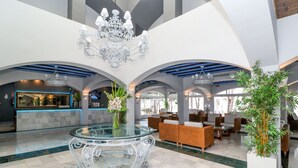 Eine großzügige Lobby mit einem Glastisch, stilvollen Kronleuchtern und gemütlichen Sitzbereichen.
