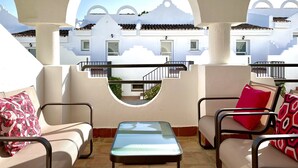 A sunlit outdoor seating area with a glass-top table, cushioned chairs, and a view of a white building with balconies. - Modern duplex 6303 - great facilities onsite (Marbella)