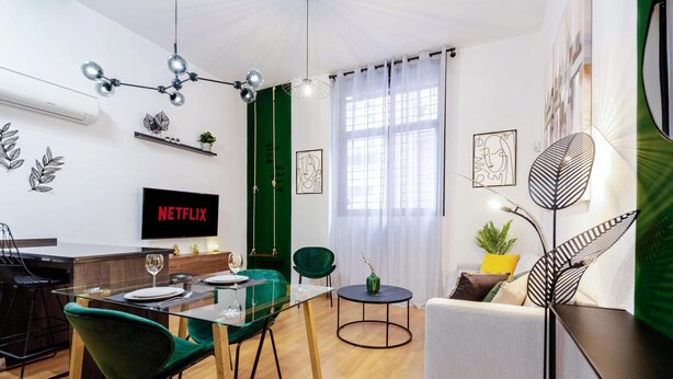 Un salon moderne comprenant un coin repas, un mur d’accent de couleur verte et un téléviseur affichant le logo « NETFLIX ».