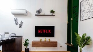 Un salon moderne avec un téléviseur fixé au mur qui affiche le logo « NETFLIX », un meuble en bois en dessous et un mur d’accent de couleur verte.