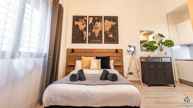 Une chambre à coucher moderne avec une tête de lit en bois, un lit recouvert de linge de lit blanc et une œuvre d’art représentant une carte du monde au-dessus.