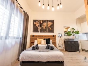 A modern bedroom with a wooden headboard, a bed with white bedding, and a world map artwork above it.