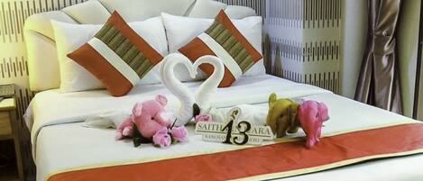 A neatly made bed with a decorative swan pillow arrangement, a number '13' sign, and a 'SAITHARA' sign on the bedspread.