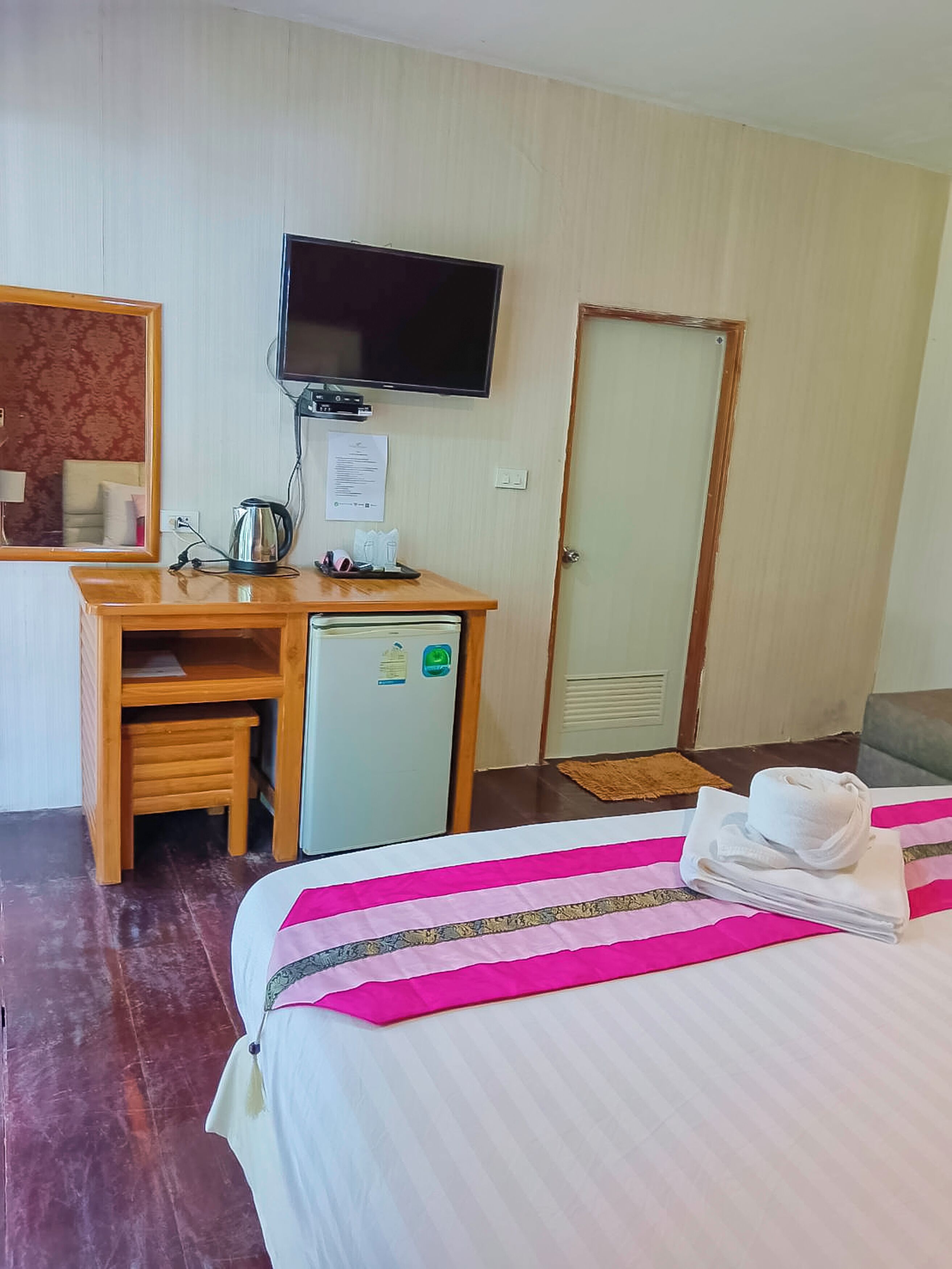 Une chambre d’hôtel comprenant un lit, un bureau avec une télévision, un petit réfrigérateur et un miroir.