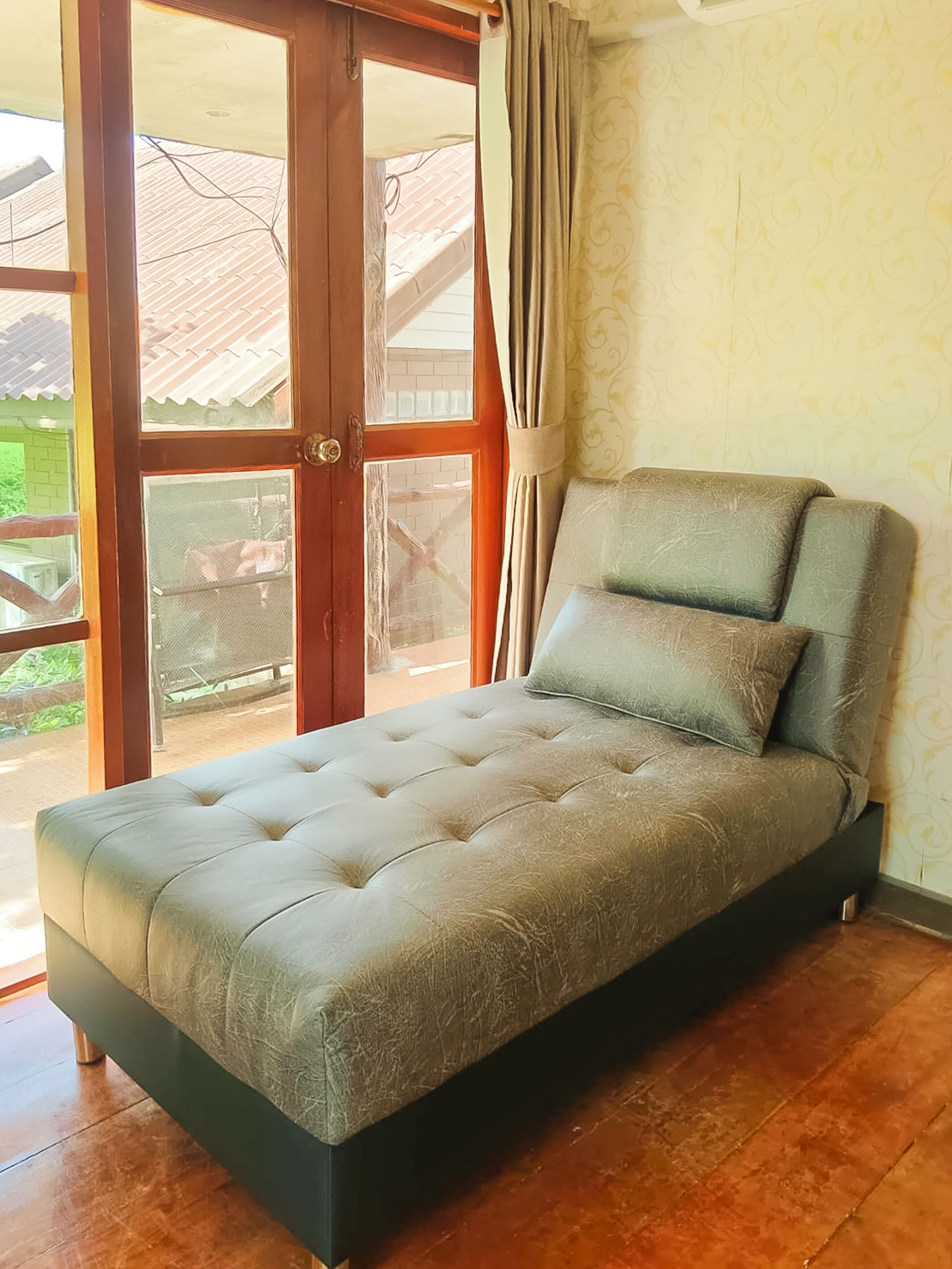 A single bed with a tufted headboard and footboard, positioned against a wall with patterned wallpaper.