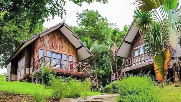 A rustic wooden cabin with a balcony, surrounded by lush greenery and a stone pathway leading to it. - Saitharn Iyara Resort (Sai Yok)