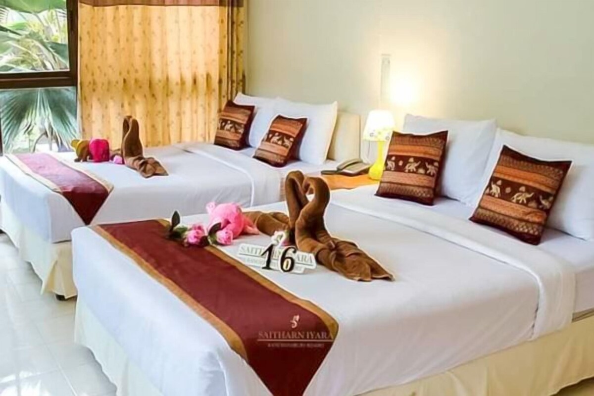 A hotel room with two beds, each with a red and white bedspread, pillows with a patterned design, and a small sign on the bed.