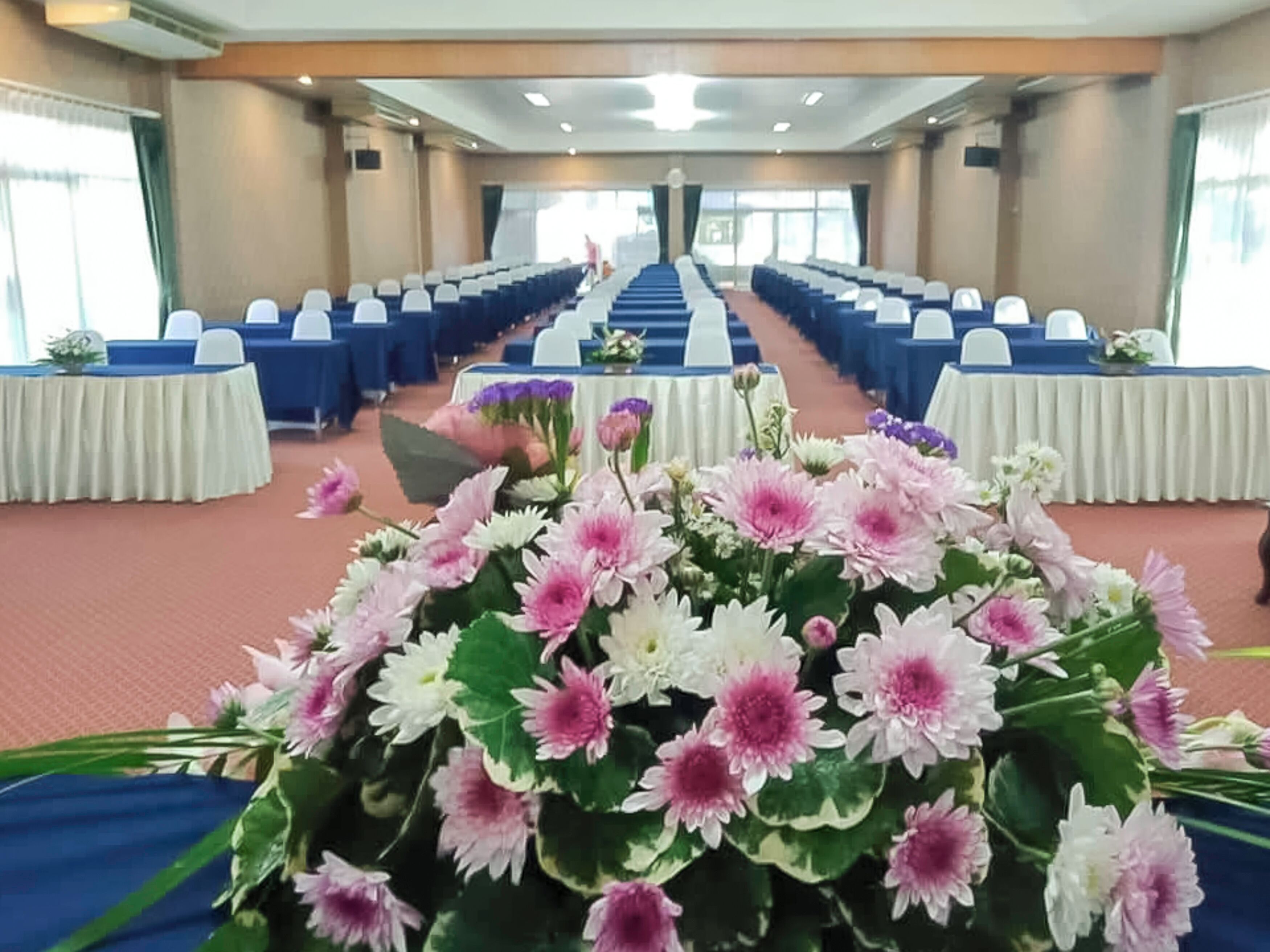 A conference room with rows of blue chairs, white tables, and a floral centerpiece.