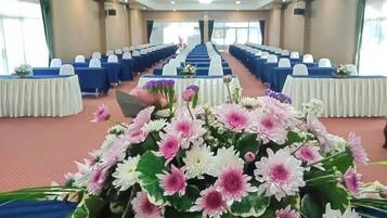 A conference room with rows of blue chairs, white tables, and a floral centerpiece.