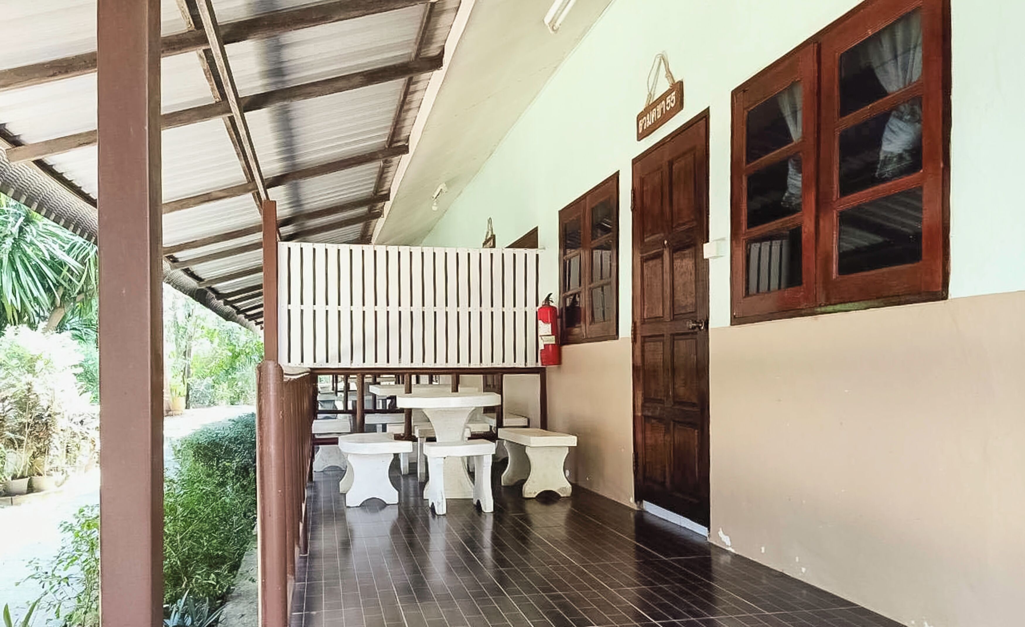 A covered outdoor area with a wooden balcony, white tables, and a fire extinguisher.