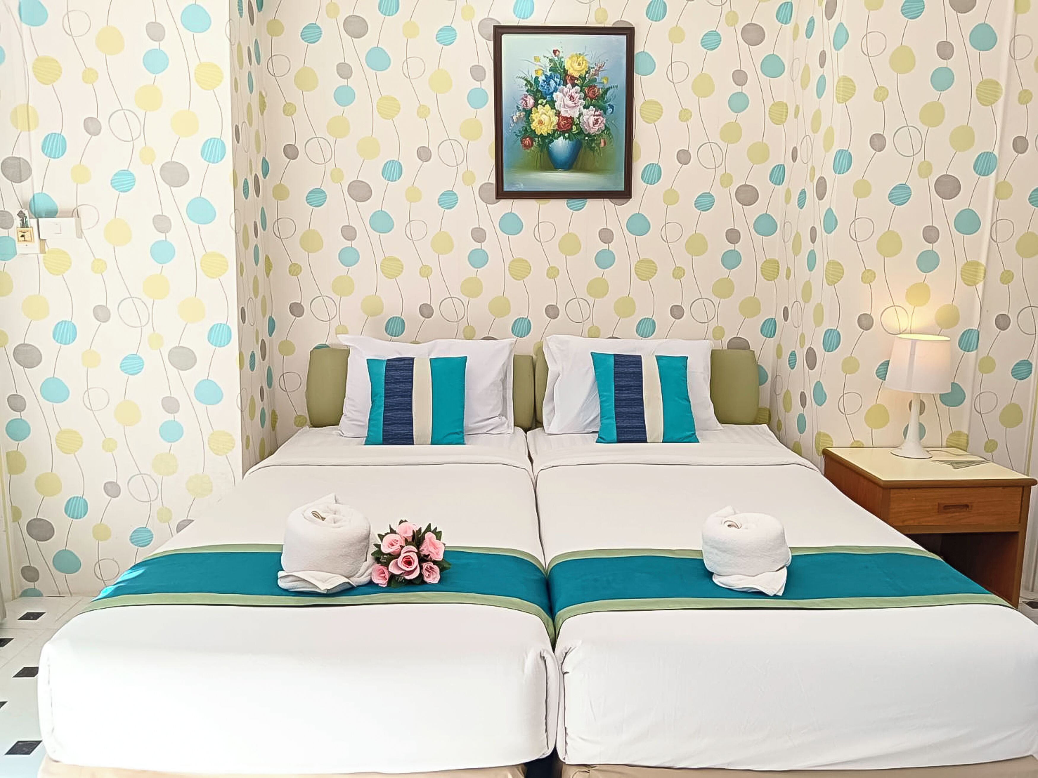 Habitación doble con dos camas, cada una con un corredor de cama color turquesa, ropa de cama blanca y almohadas color turquesa. En la pared, sobre las camas, hay una obra de arte floral enmarcada.