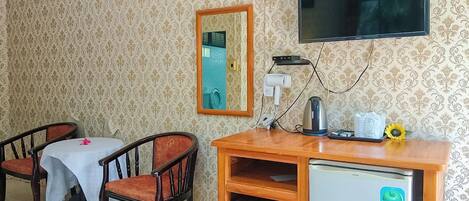 Een kamer met een televisie, een kleine koelkast, een tafel met stoelen en een spiegel aan de muur.
