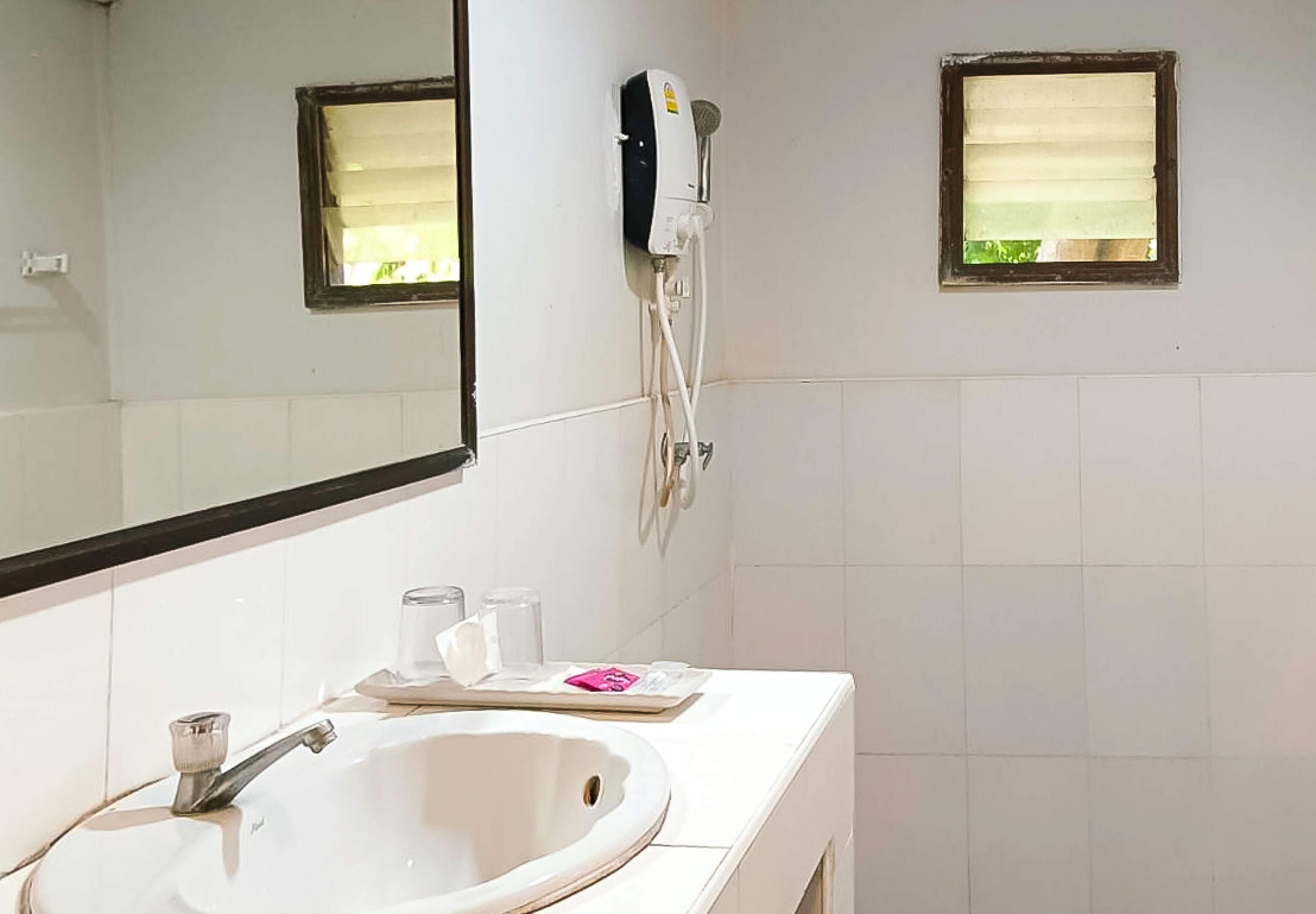 A bathroom with a white sink, a mirror, a handheld showerhead, and two small windows.