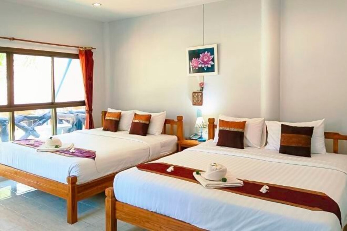 A hotel room with two beds, a window with curtains, a wall-mounted picture, and a small table with a lamp.
