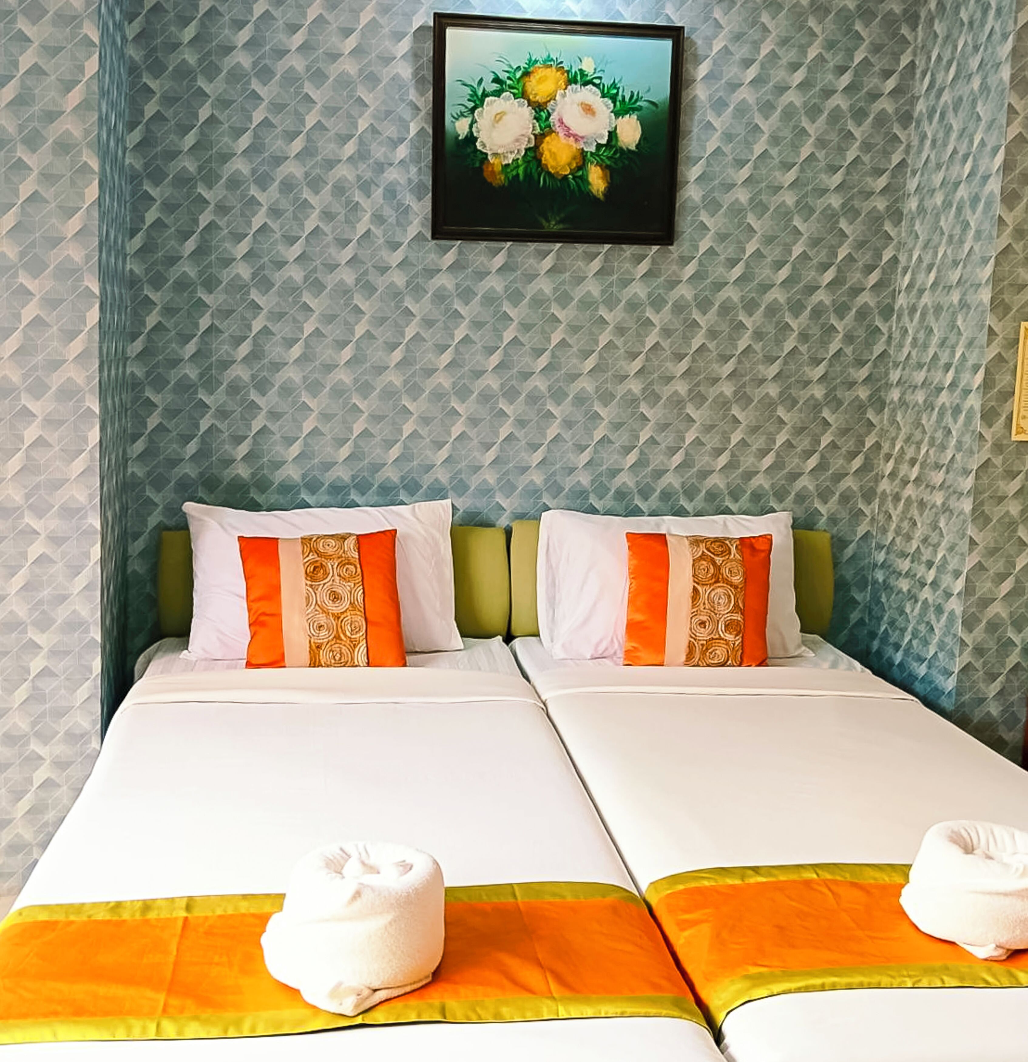 A hotel room with two beds, each with white bedding and orange accents, a green headboard, and a framed floral artwork on the wall.