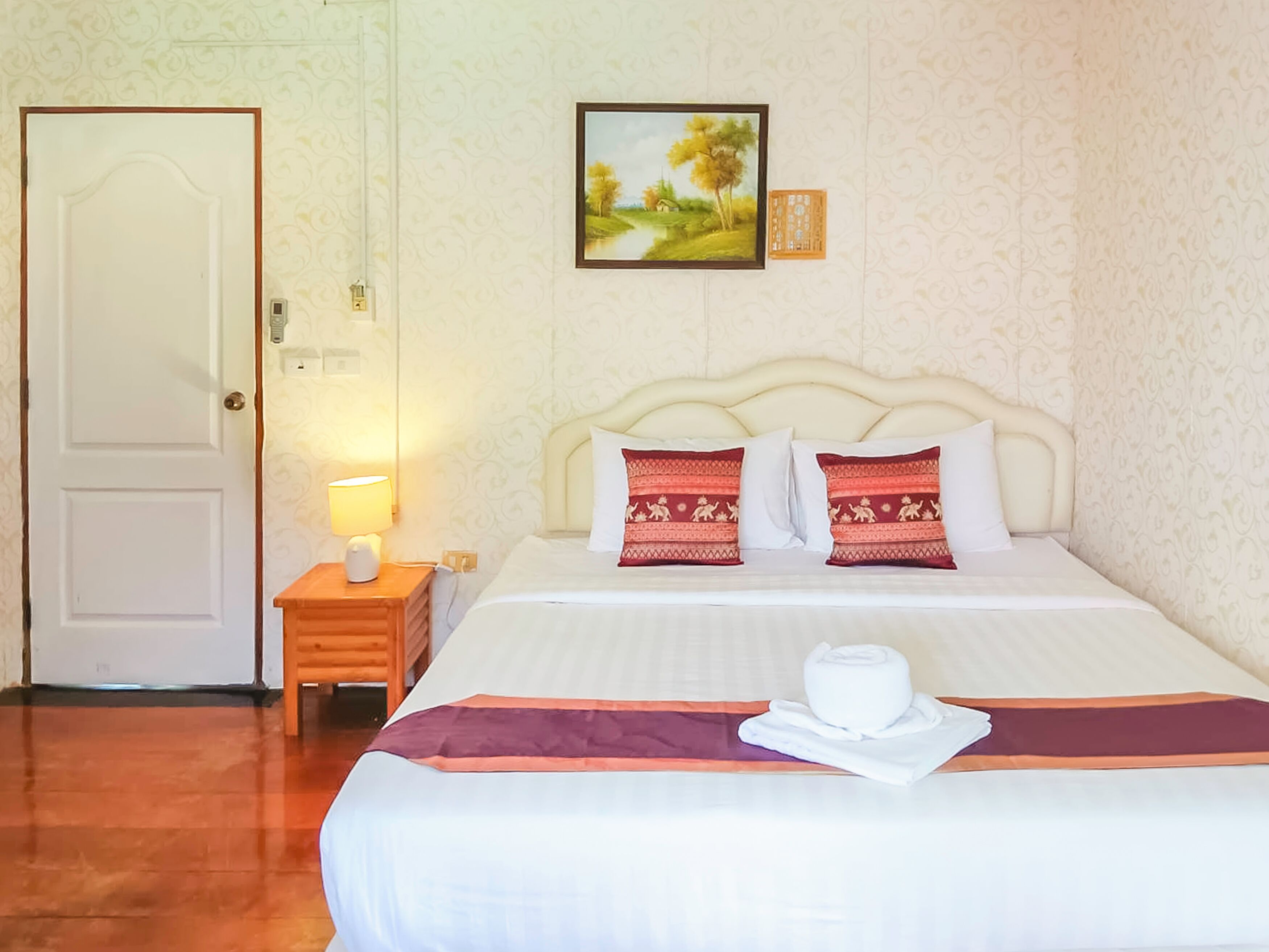 Una habitación de hotel con una cama, una mesita de noche con lámpara, un cuadro en la pared y una puerta.