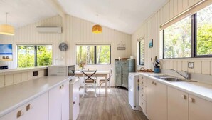 Une cuisine moderne avec des meubles blancs, un coin repas comprenant une table et des chaises, et de grandes fenêtres offrant une vue sur la verdure.