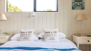 Un lit bien fait, avec une literie à rayures, deux oreillers ornés de motifs, une lampe de chevet, une table de chevet et une fenêtre donnant sur un paysage verdoyant.