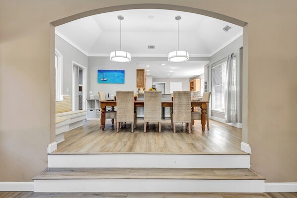 Un coin repas avec une table et des chaises en bois, un luminaire au plafond et une vue sur une autre pièce.