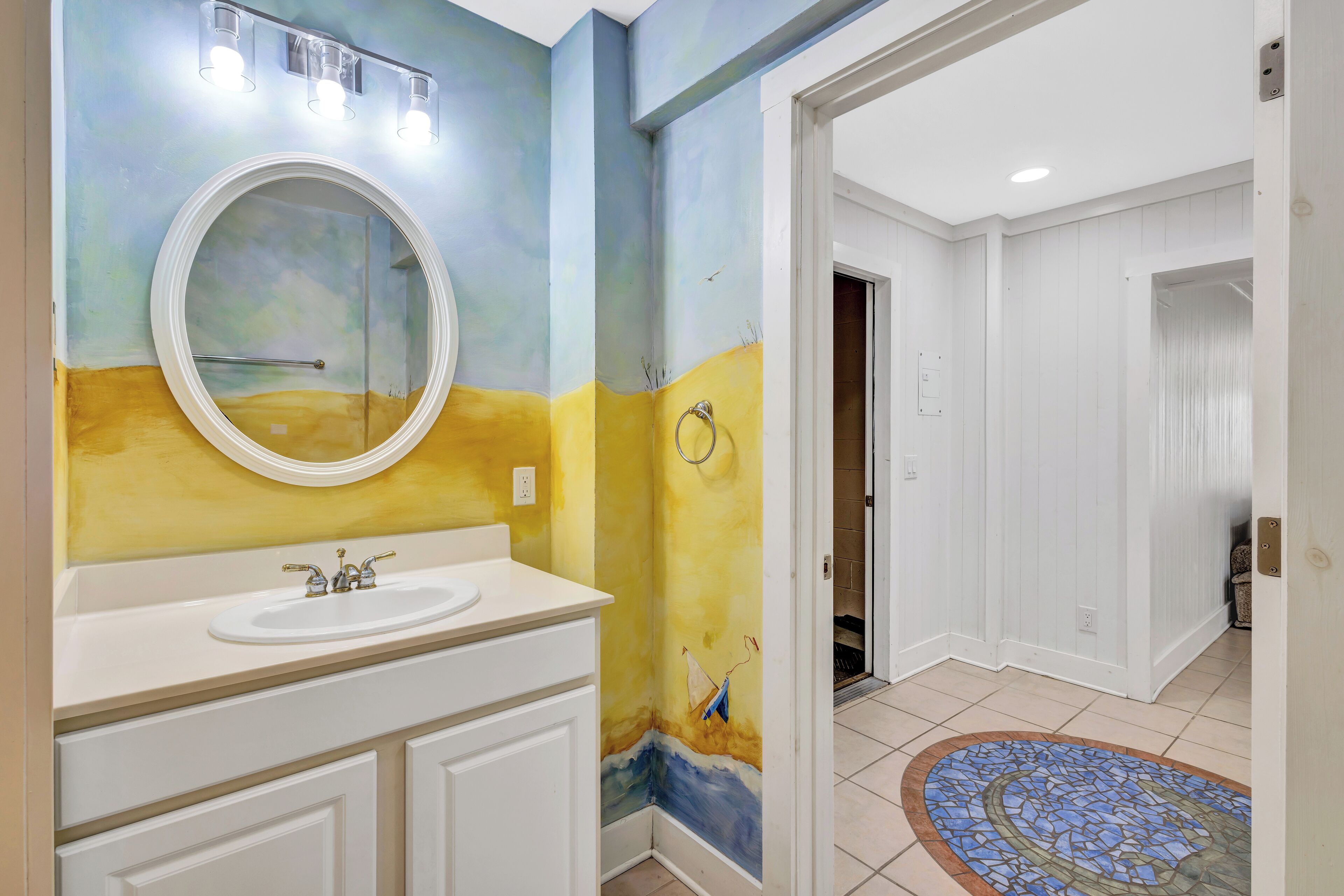 A bathroom with a round mirror, a sink, and a tiled floor.