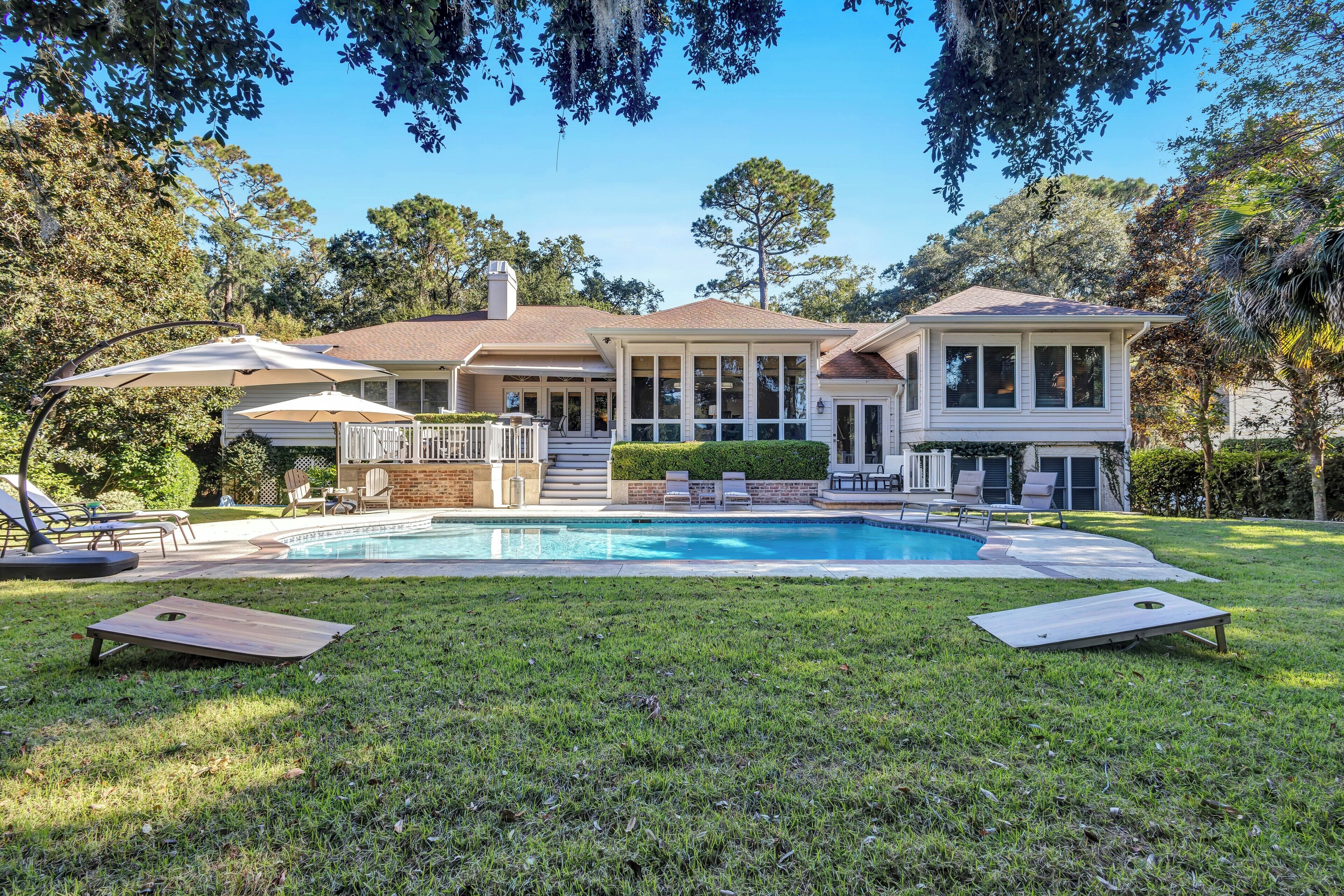 Une maison à deux étages avec une piscine, un patio couvert et une pelouse aménagée avec du mobilier d’extérieur.