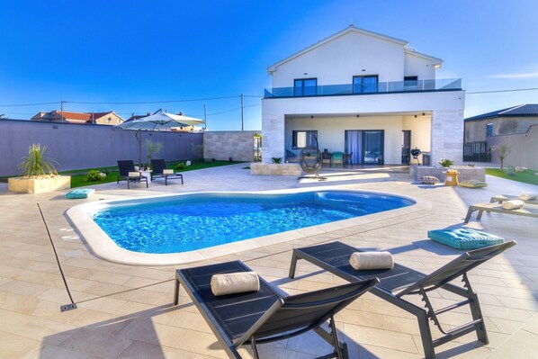 Ein modernes Haus mit Swimmingpool, Sitzgelegenheit im Freien und einem gepflegten Garten.