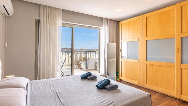 Et hotelværelse med seng, garderobeskab, balkon med udsigt og aircondition.