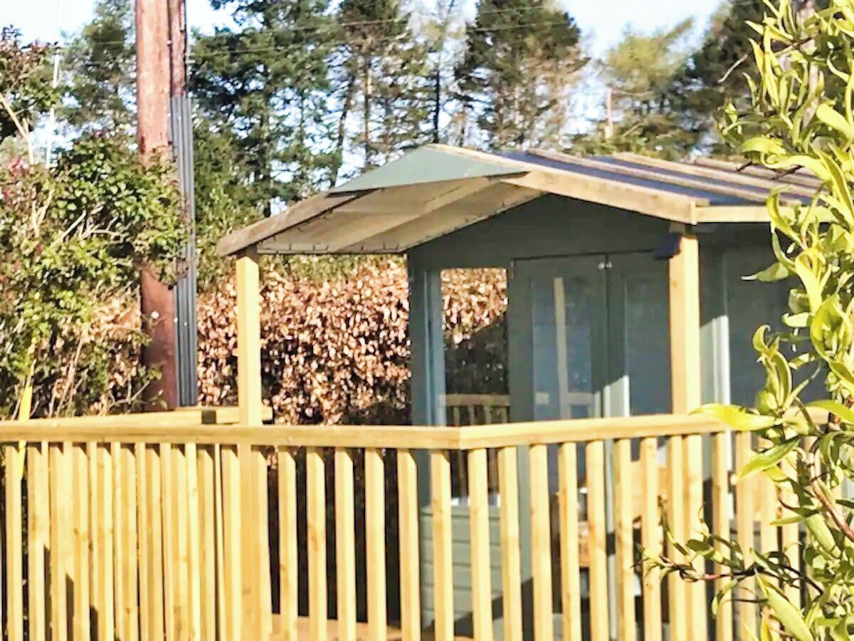 A wooden deck with a covered seating area, surrounded by trees and foliage.