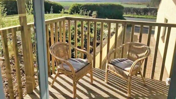 Eine Holzterrasse mit zwei Korbstühlen und einem Metallgeländer.