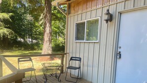 A wooden deck with two chairs and a table, a door with a window, and a tree in the background. - Whispering Pines (Redmond)